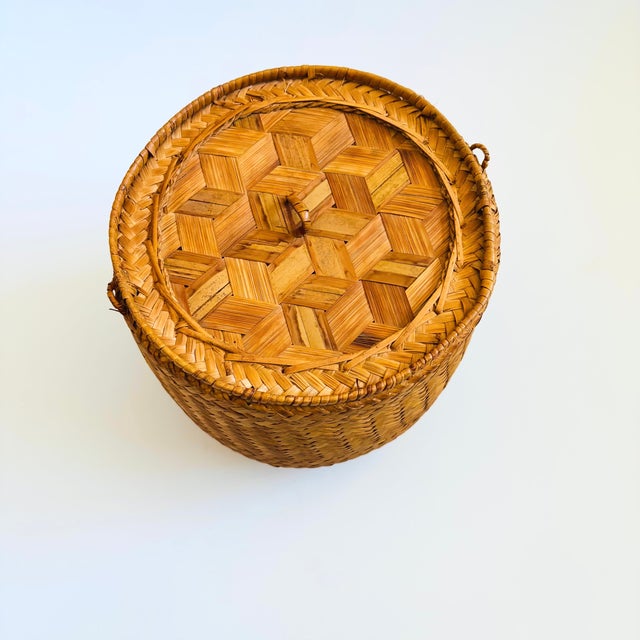 A vintage lidded wicker basket in a cylinder shape and with a sleeve style lid.