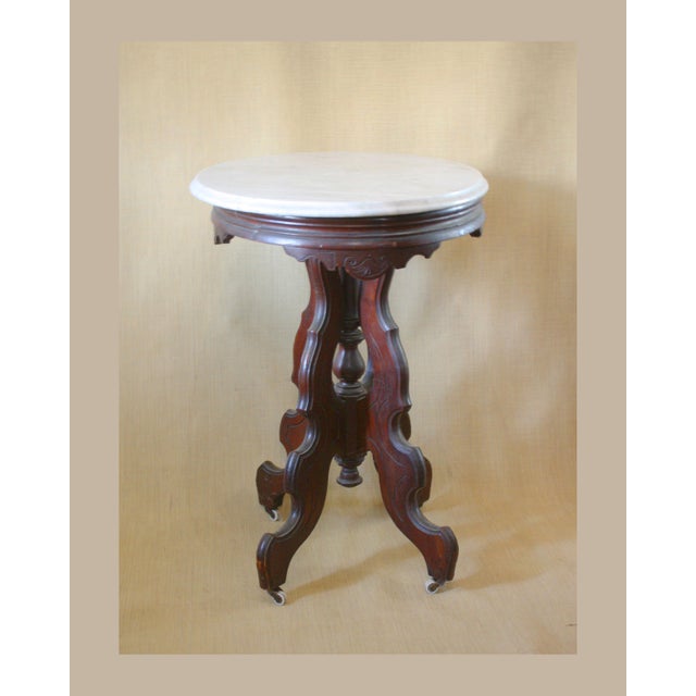 This antique Victorian center table has a beveled marble top and carved mahogany base. The four legs radiate from a...