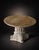 A dramatic round dining table featuring a polished natural stone top and an elaborately detailed pedestal base. The...