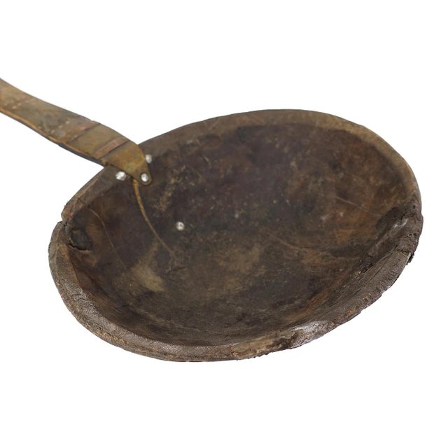 A large spoon or scoop made out of wood carved with a large bowl and a long handle with aluminum designs. This spoon is...
