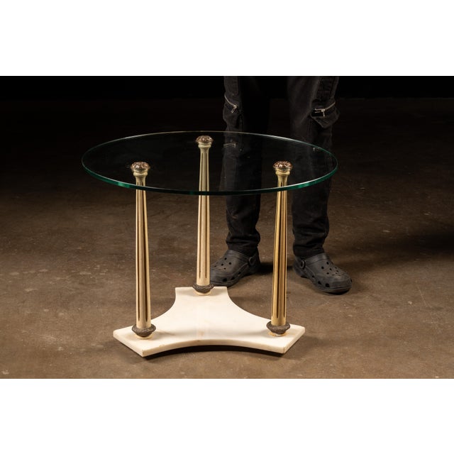 Vintage round side table featuring a circular tempered glass top supported by three tall, fluted wood columns rising from...