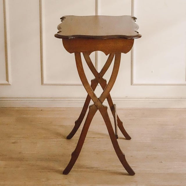 A side table from around 1900, crafted from mahogany and beech, with a curved top and characteristic X-shaped frame. The...