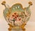 A scalloped, footed porcelain jardinière with heavy gilt scrollwork along the rim, handles, and feet, set against a soft...