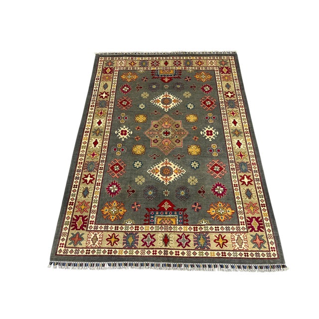 A deep gray field showcases a central star medallion surrounded by smaller Kazak motifs in burgundy, gold, blue, cream,...