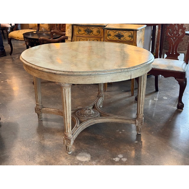 Center table in the Louis XVI style with a painted and faux-marble top over fluted legs joined by an arched X-stretcher....