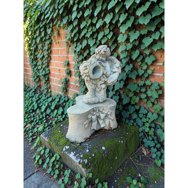 A beautifully sculpted antique-style cherub garden fountain figure, resting against a tipped urn and mounted on an ornate...
