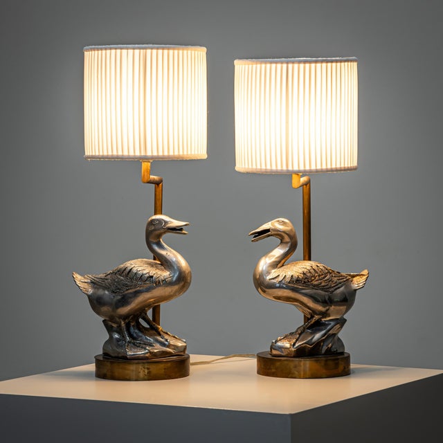 Pair of metal table lamps with cylindrical pleated fabric shades. Each rests on a round base featuring fully sculpted...