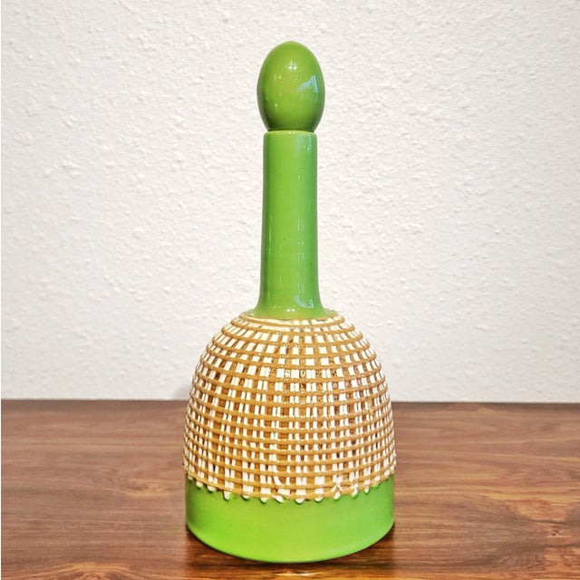 A bright green, pop-era decanter and stopper with a latticework skirt of thick, white-and-butterscotch “icing” from the...