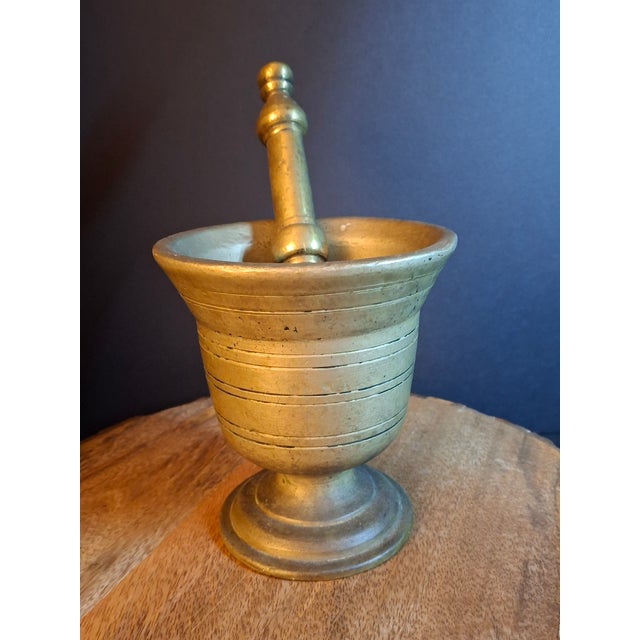This heavy 18th-century cast brass mortar and pestle showcases classic lathe-turned concentric incised ring detailing...
