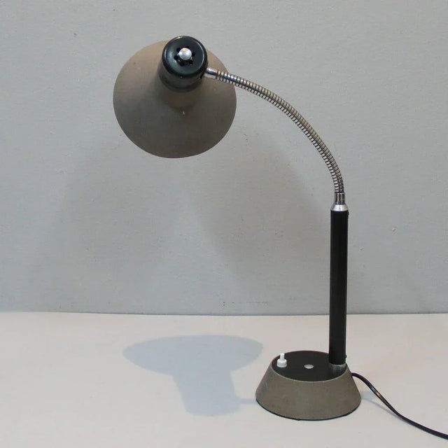 This metal lamp in a gray color with chrome and black plastic on the arm retains its vintage patina and uses a B22 cap....