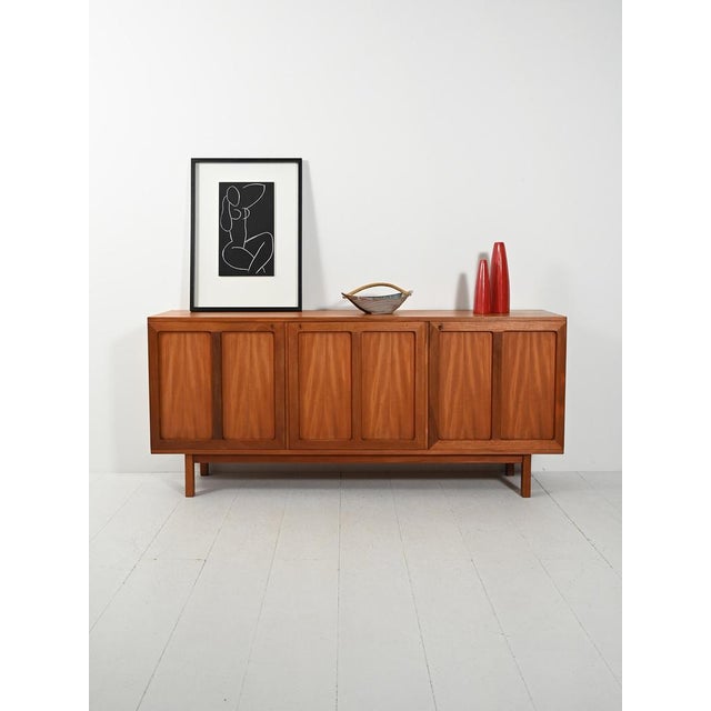 Elegant Swedish teak sideboard with three relief doors; cutlery drawers on the left, linear shelves on original slender...
