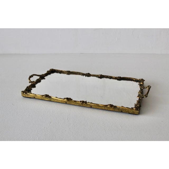 This vintage ornate brass-finish mirrored vanity tray features an intricate floral and twig-molded metal frame with dual...