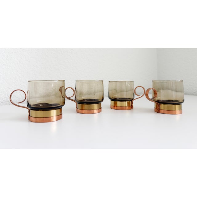 A handsome set of four espresso cups featuring mixed metal copper and brass handle/holder and smoked gray glass cups. The...