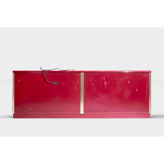 Lacquered wood sideboard finished in a vibrant high-gloss red, accented by polished brass trim and hemispherical brass...