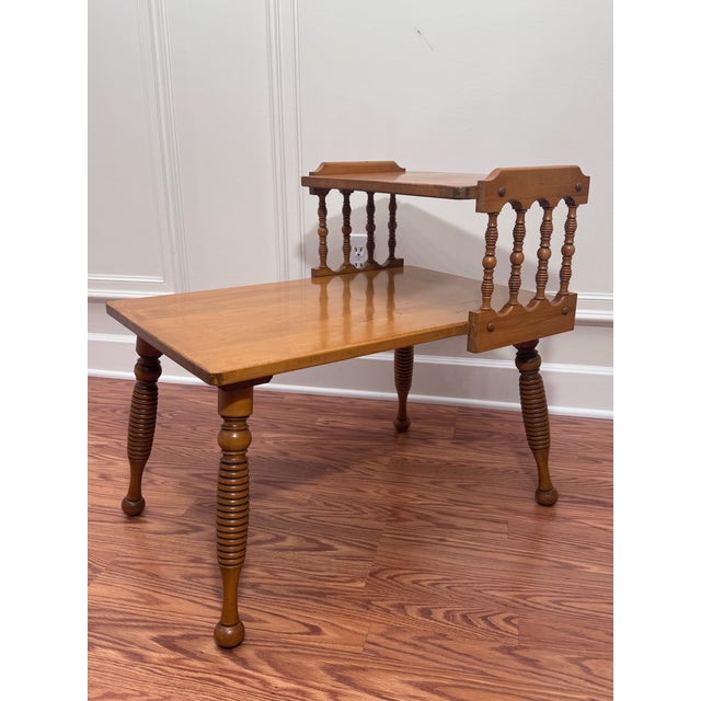 This is a vintage two tiered side table featuring a warm honey-toned finish on what appears to be solid wood maple....