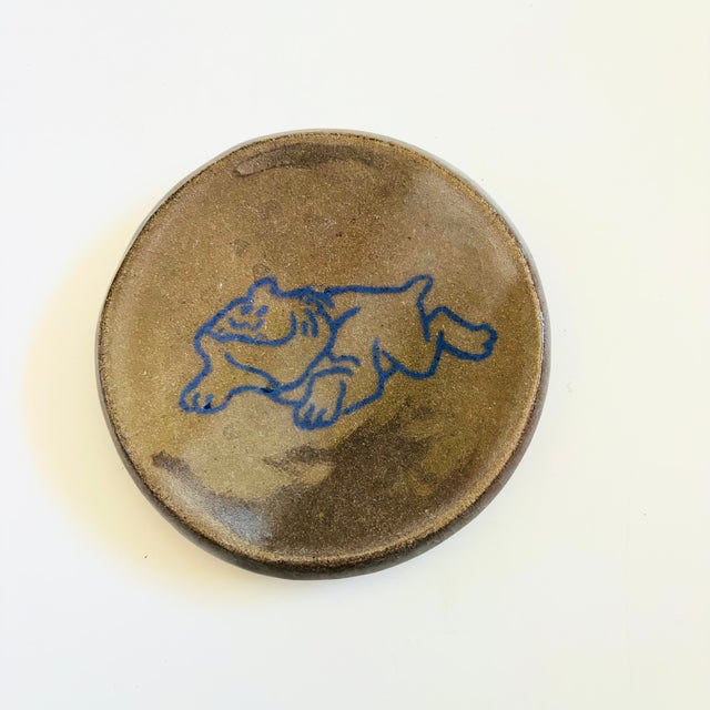 A vintage studio pottery bulldog plate. Features a blue hand painted bulldog in the center with a gray base glaze....