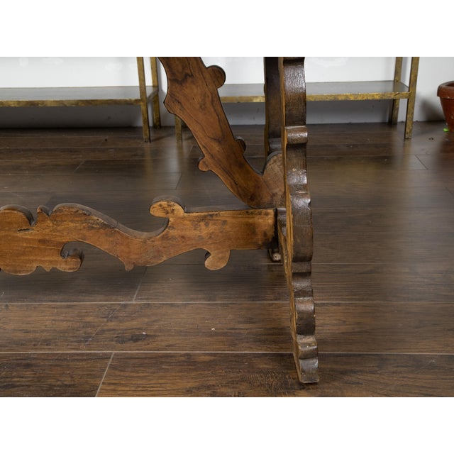 An Italian Baroque style walnut table from the 19th century, with carved trestle base and scoop motifs. Created in Italy...