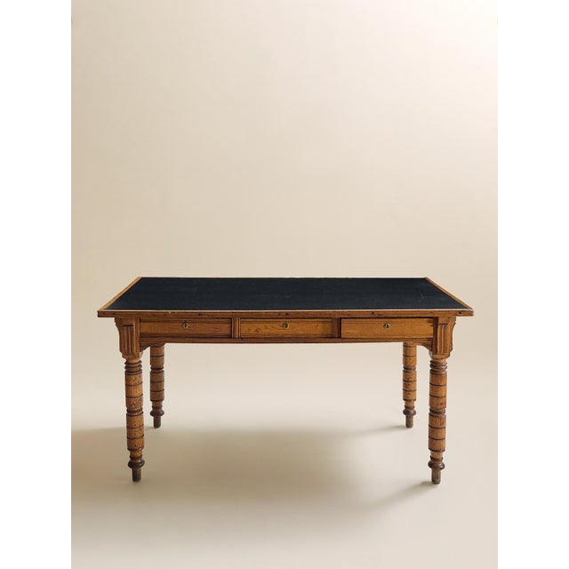 This vintage table features a warm wood frame with turned carved legs, three front drawers, and a dark leather inset top....