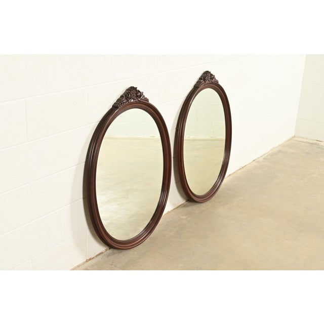 A gorgeous pair of antique Victorian or Neoclassical style carved mahogany framed oval wall mirrors In the manner of...