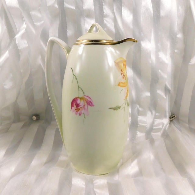 This is a white coffee pot or teapot by Schoenwald PSAG Bavaria. It is white with a pink and yellow floral design, gold...