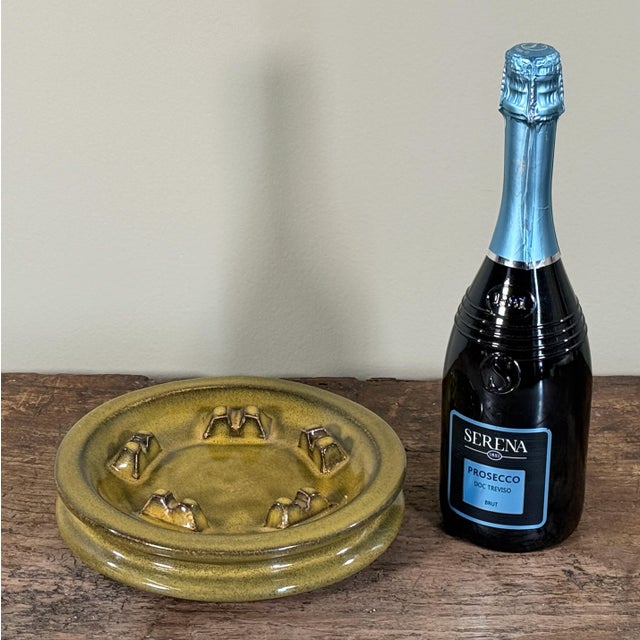 Vintage studio pottery ceramic ashtray with a mottled yellowy olive green glaze and raised cigarette rests around the rim....