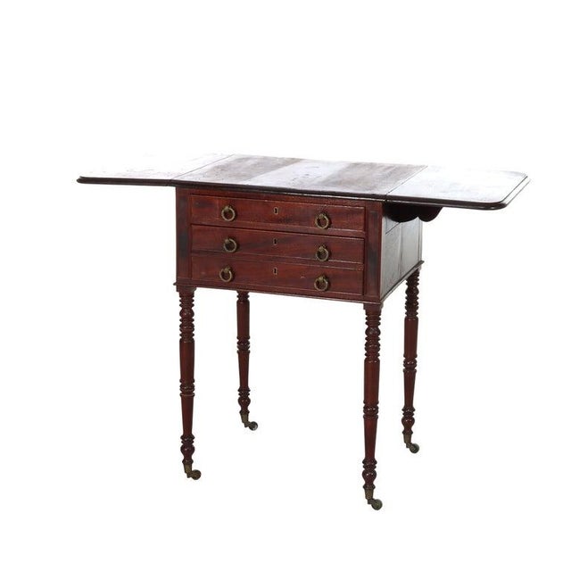 An antique Sheraton style drop-leaf sewing stand, crafted from rich mahogany and dating to approximately 1840. This...