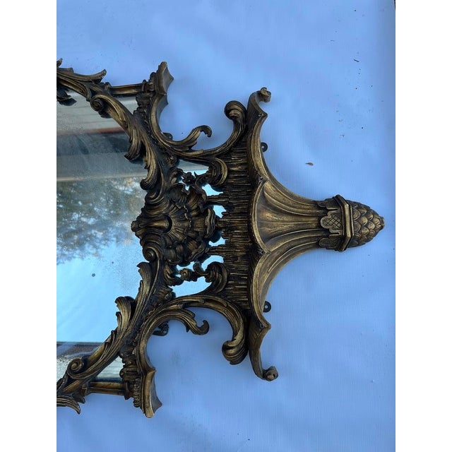 A single large antique carved wood chinoiserie style oval wall mirror featuring a gold gilt finish, stylized pagoda shaped...