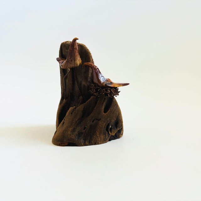 A vintage wood bird sculpture. Two carved wood birds are mounted to a natural wood base. One bird sits in a small nest....