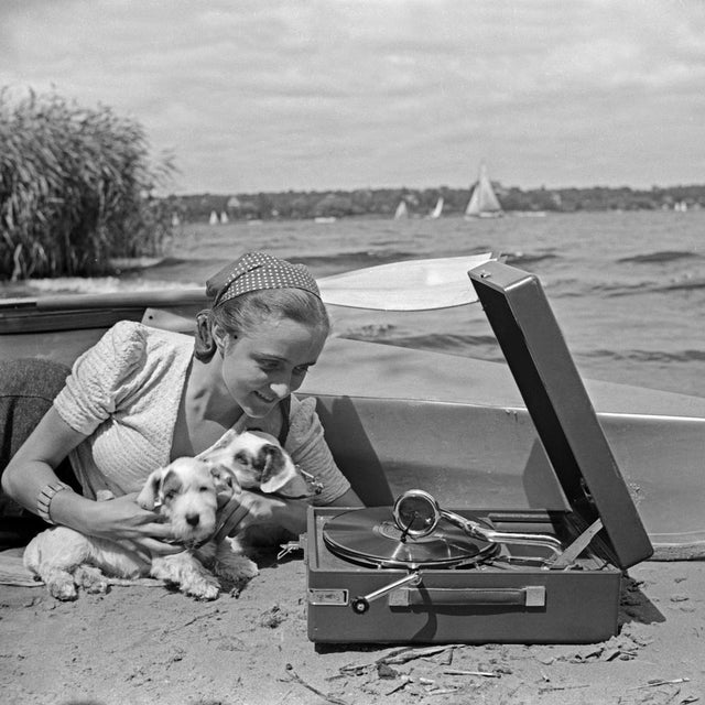 Germany, Summer 1936 – Photograph by Heinz Pollmann In this idyllic lakeside moment, captured by Heinz Pollmann in the...