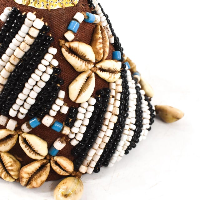This intricately handwoven hat is covered in glass beads and cowrie shells. The Kuba beaded noble's hat with cowrie shells...