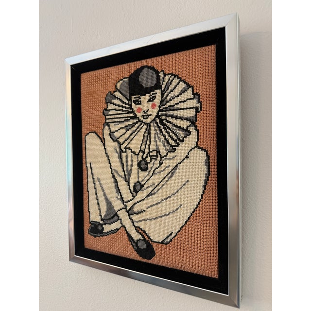 Vintage framed needlepoint artwork depicting a seated Pierrot clown with a large ruffled collar on a textured salmon-pink...