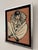 Vintage framed needlepoint artwork depicting a seated Pierrot clown with a large ruffled collar on a textured salmon-pink...