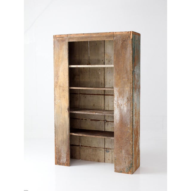 An antique primitive cupboard with an open shelving form, defined by tall proportions and a layered painted surface that...