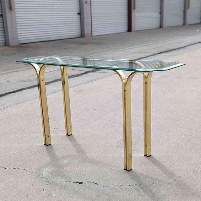Vintage Brass and Glass Console Table. A slender vintage console table with a beveled glass top and polished brass-toned...