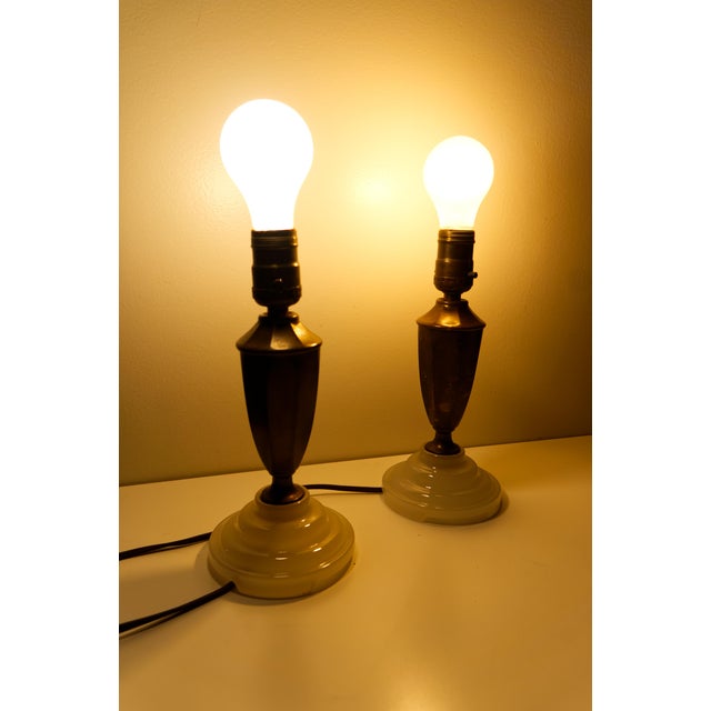 A pair of vintage small brass table lamps featuring elegant urn-shaped silhouettes and luminous opal glass bases. Their...