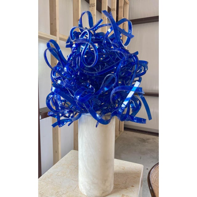 Whimsical heat formed ribbons of cobalt blue acrylic woven together and mounted upon a cylindrical marble base.
