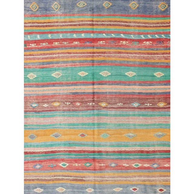Featuring geometric tribal shapes rendered in a repeating horizontal stripe design, this unique midcentury Kilim showcases...