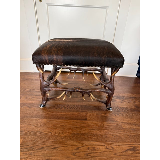 Rustic stool by Theodore Alexander showcases a base of high-strength composite “antlers”, hooved feet, and faux hair on...