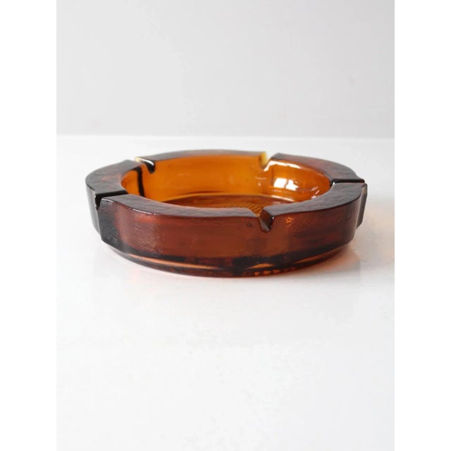 This vintage amber glass ashtray features a bold Federal eagle design at the center and includes five rests for cigars or...