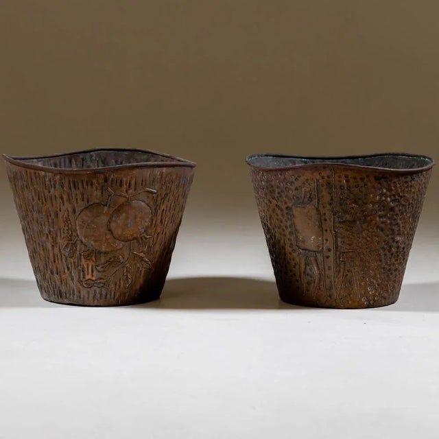 Pair of copper plant pots with relief walls and wavy rim. One pot shows stylised warriors, the other pomegranates.