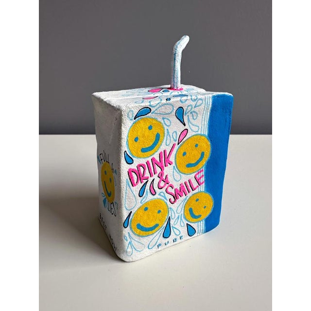 Small-scale clay sculpture in acrylic explores consumption through a juice-carton object, pairing sugar and pill imagery...