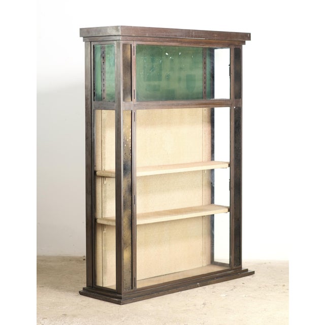Vintage brass free standing display case with glass sides and doors. The upper cabinet has a green interior, while the...