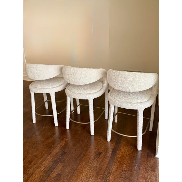 A stunning set of three Hagen counter stools featuring sculptural lines, plush ivory bouclé upholstery, and an elegant...