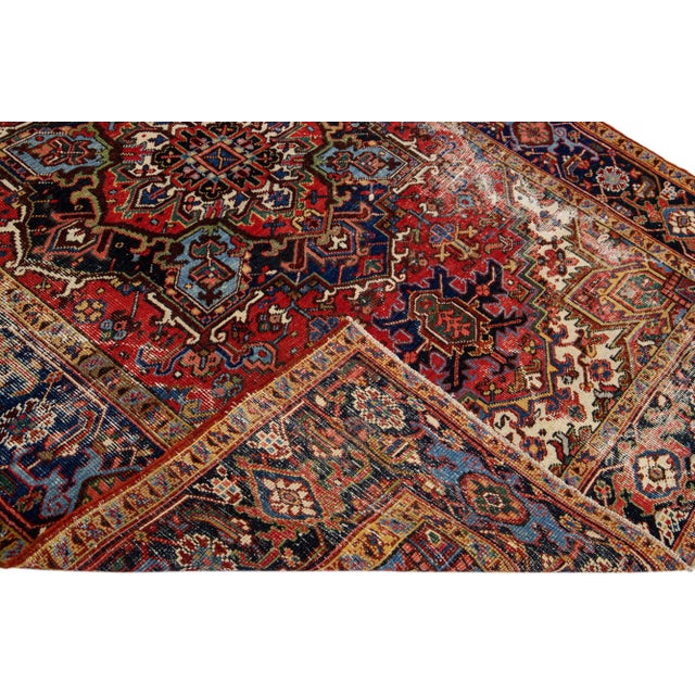 Beautiful antique Heriz hand-knotted wool rug with a red field. This Heriz rug has a navy-blue frame and multi-color...