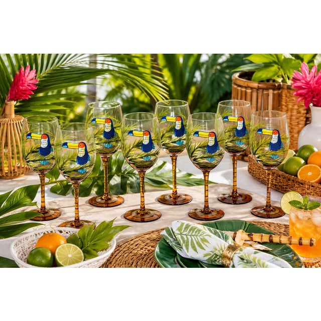 A vibrant set of seven hand-painted wine glasses featuring colorful toucans perched among lush tropical foliage. Each...