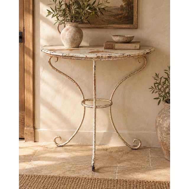 A characterful vintage demi-lune console table combining a decorative wrought iron base with a heavily distressed painted...
