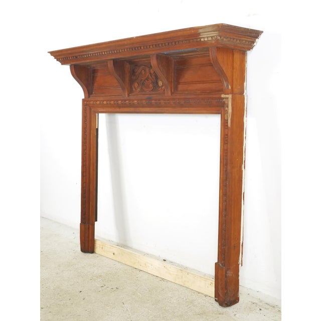 Victorian style wood fireplace mantel with a dark stain. It features a central carved frieze with scrolling ribbons around...