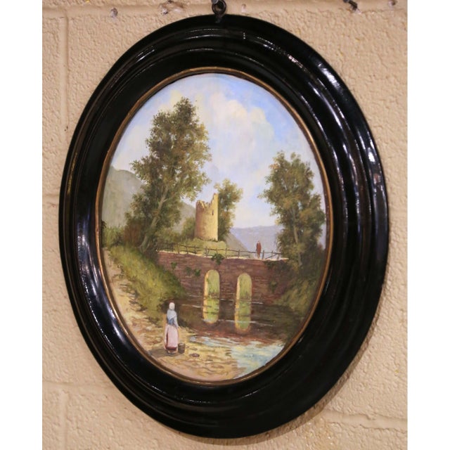 This charming antique landscape painting captures a peaceful rural scene with a stone bridge, architectural ruins,...