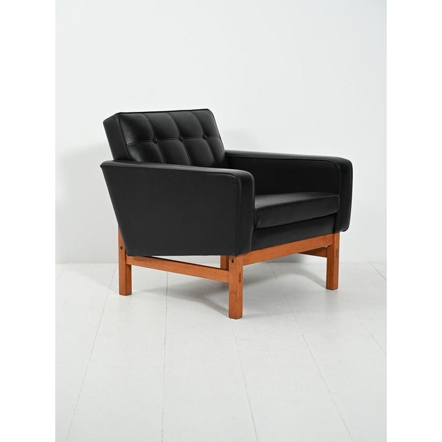 Swedish armchair by AB Futura from the 1960s/70s in black faux leather with teak legs, square volumes, and enveloping...