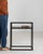 Black metal-framed side table with glass top and shelf in Blackened Iron. Its blackened iron finish sets off minimalist...